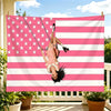 A woman is swinging on a large American flag tapestry featuring red, white, and pink stripes and stars.