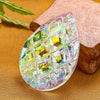 A faceted crystal prism with green and yellow hues rests on a piece of natural fabric.