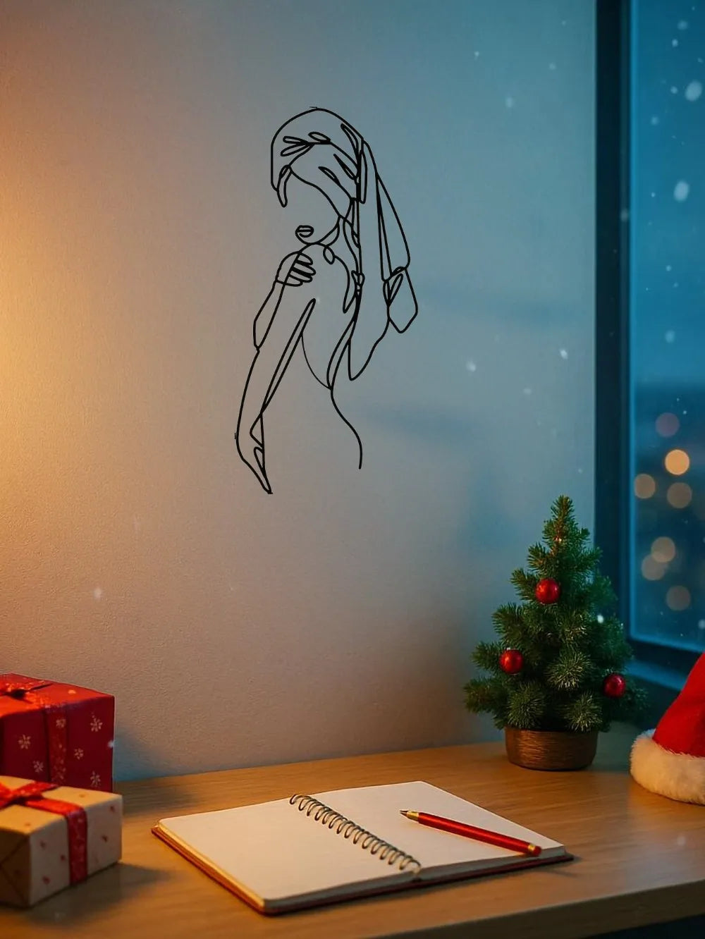 A black line art silhouette of a girl with hair covering her face on a white wall next to a notebook and wrapped gifts.