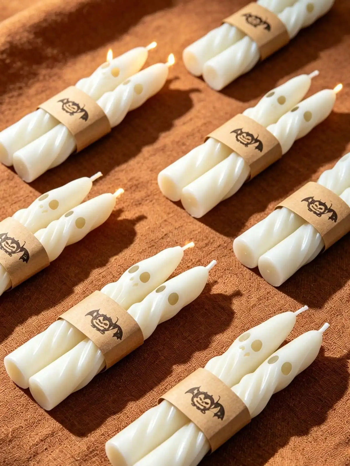 A set of white soy candles wrapped with brown paper and featuring a Halloween ghost design.
