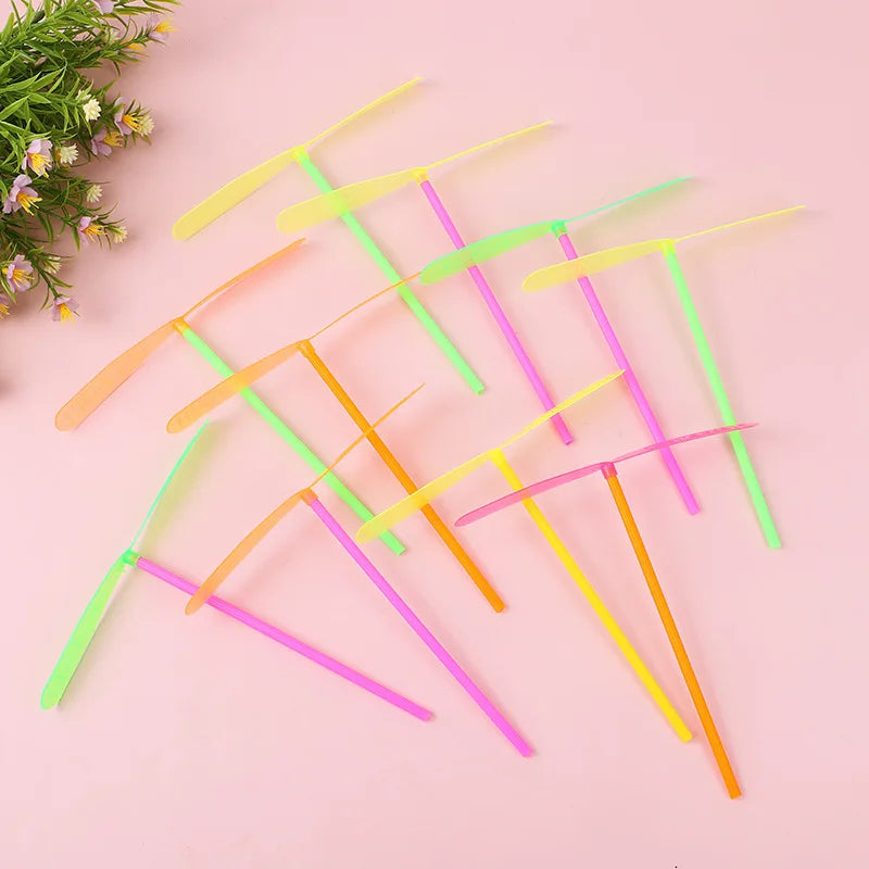 A collection of colorful bamboo dragonfly flying propeller toys arranged diagonally on a pink background.
