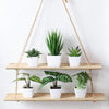 A set of six small artificial flower bonsai plants in white pots hanging from a macrame hanger on a wooden shelf.
