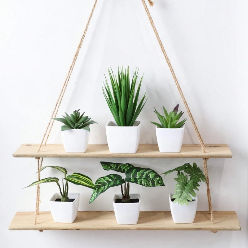 A set of six small artificial flower bonsai plants in white pots hanging from a macrame hanger on a wooden shelf.