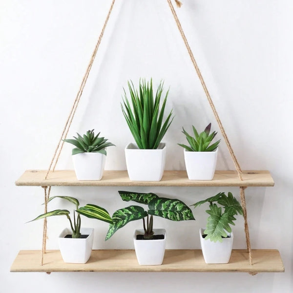A set of six small artificial flower bonsai plants in white pots hanging from a macrame hanger on a wooden shelf.