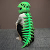 Un jouet en peluche ressemblant à un squelette de dinosaure, de couleur vert néon vif, est exposé sur un fond gris.