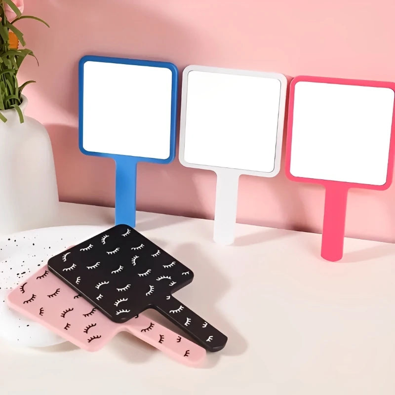 A set of three rectangular vanity mirrors with colored frames and a black handheld mirror with a pink handle