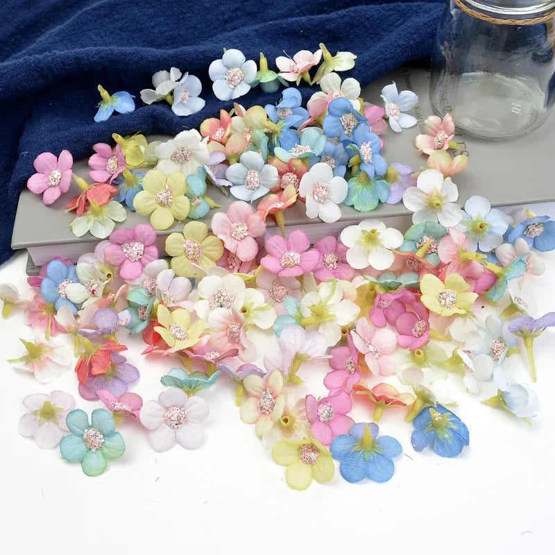 A collection of silk artificial flower heads in various pastel shades of pink, blue, and white scattered on a gray surface.