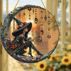 A decorative stained glass window featuring a witch figure in a pointed hat and green dress with hanging jewels.