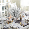 A bouquet of silvery-green artificial eucalyptus leaves displayed in a glass vase on a dark wooden table.