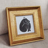 A gold-framed photograph featuring a black and white drawing of a person sitting with their head bowed.