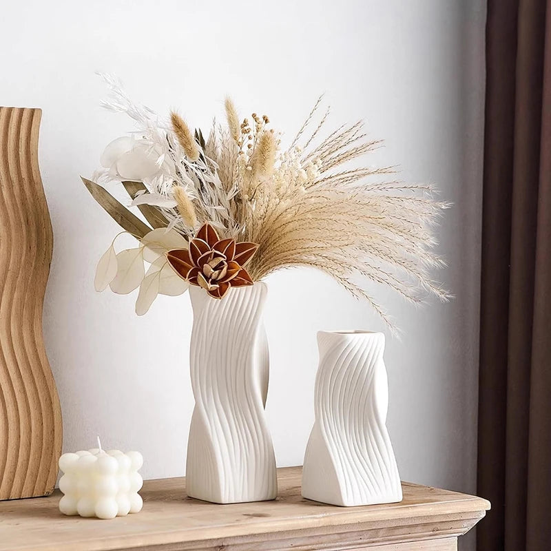 A modern white plastic decorative vase holds dried floral arrangements and natural elements on a wooden surface.