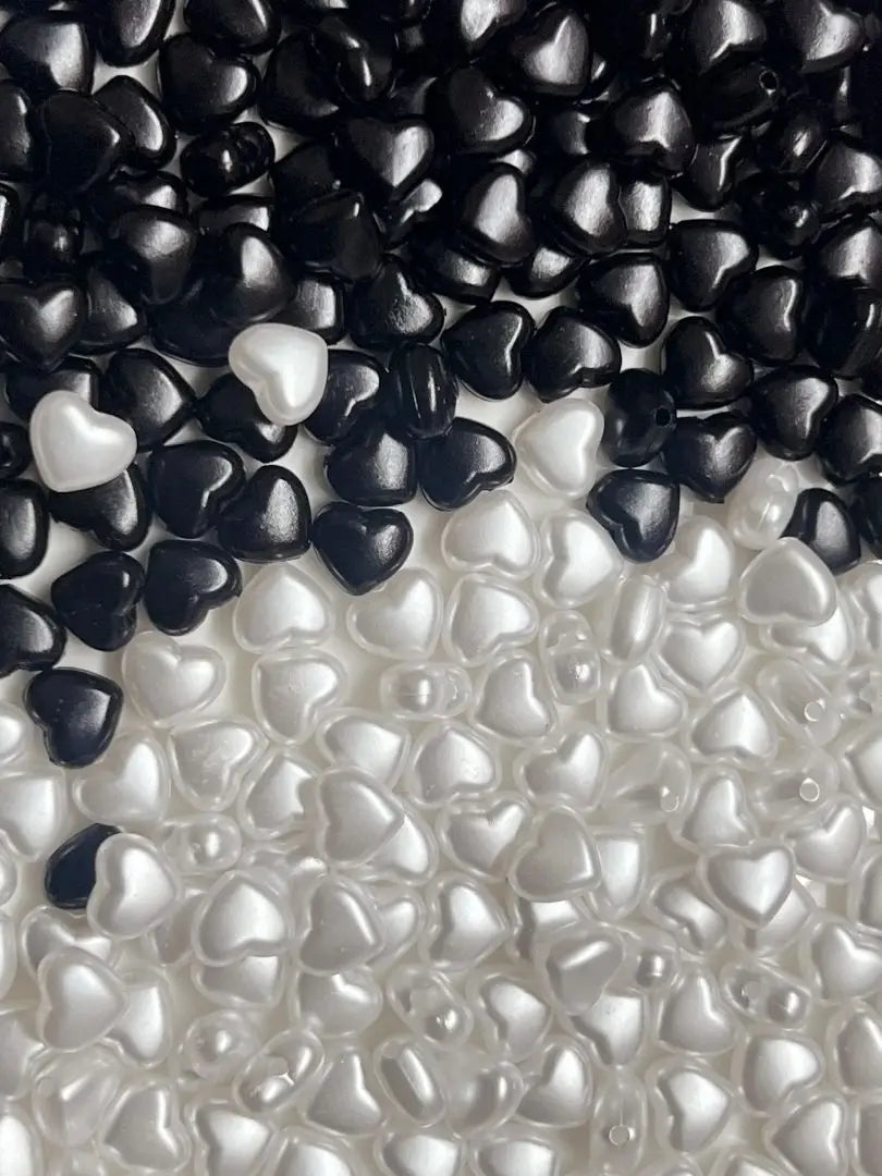 A close-up of black and white heart-shaped acrylic beads scattered on a white surface.