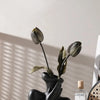 A black ceramic figural vase shaped like a hand holding a dried olive leaf, displayed on a light surface.