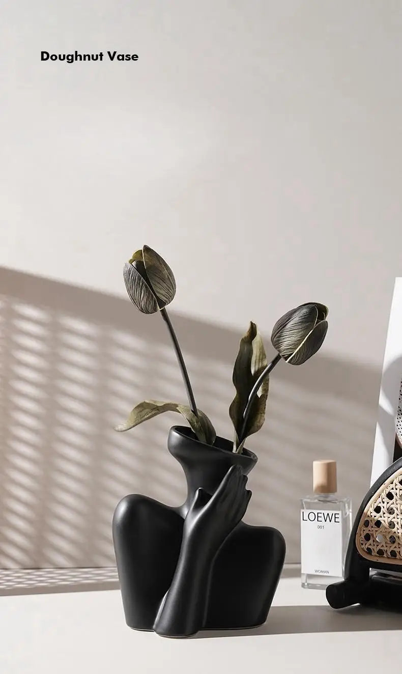 A black ceramic figural vase shaped like a hand holding a dried olive leaf, displayed on a light surface.