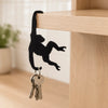 A black monkey-shaped storage hook with a banana design hanging from a keyring, mounted on a wooden shelf.