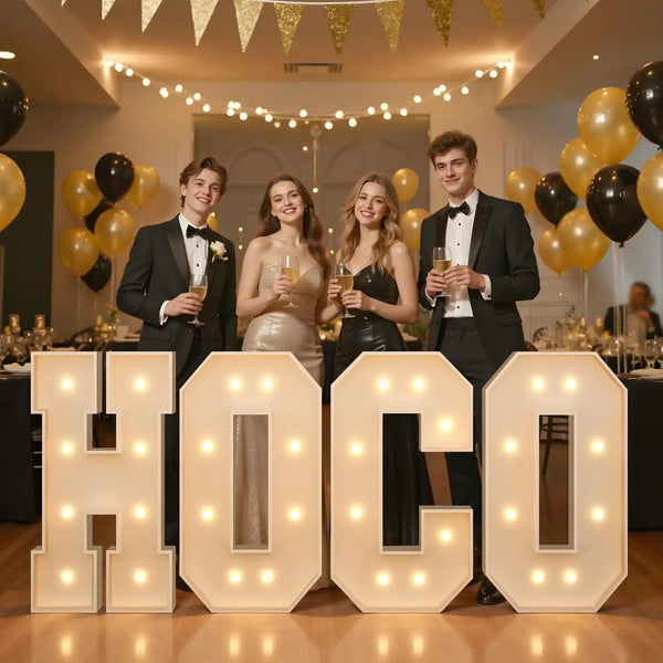 Five young adults posing in front of large marquee light-up letters spelling H O C O for a party decor event.