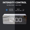 A digital alarm clock display showing 12:00 in a dark mode setting with a bright sunlight icon above.