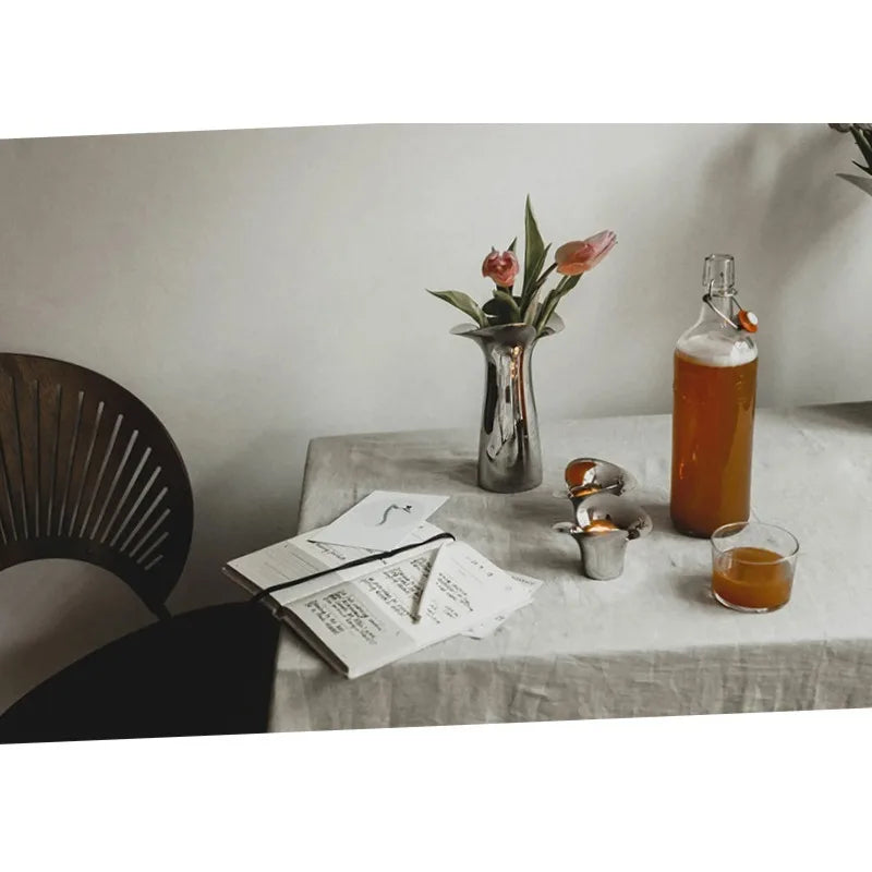 A silver-plated ceramic vase with Nordic floral design sits on a table next to a glass of amber liquid.