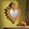 Ornate gold-framed heart-shaped wall mirror with a flame design mounted on a lime green textured wall.