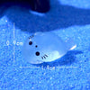 A translucent blue glow in the dark resin sea animal figurine with black features resting on a bright blue surface.