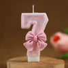 A pink number seven candle decorated with glitter and a pink bow, set against a brown background.