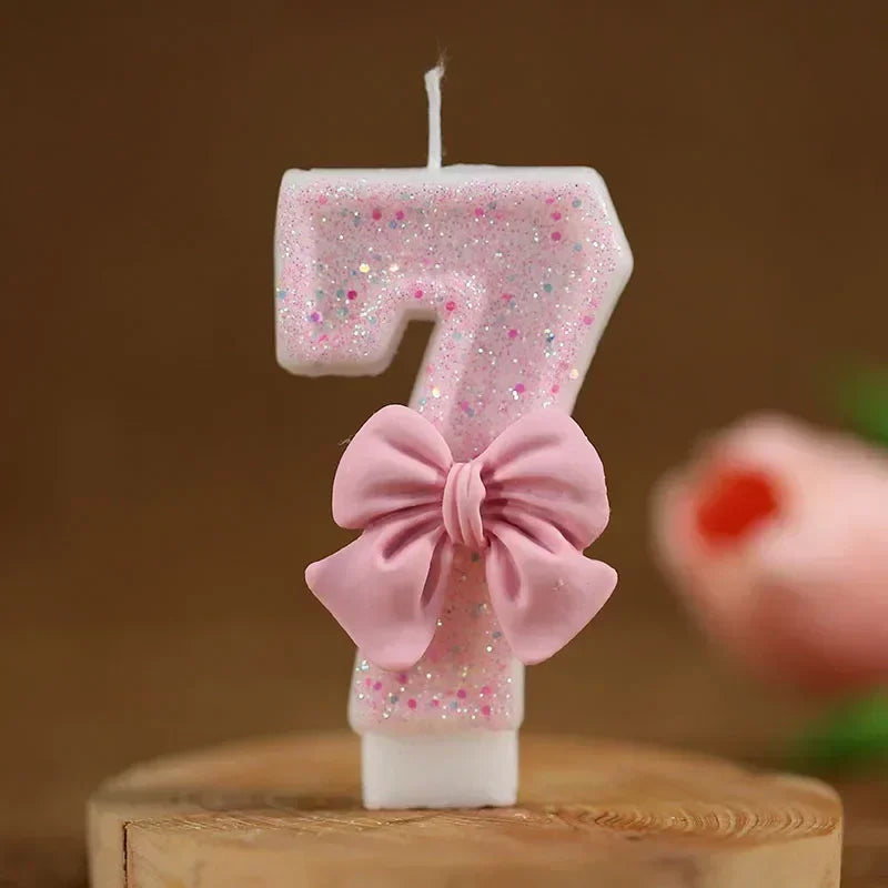 A pink number seven candle decorated with glitter and a pink bow, set against a brown background.