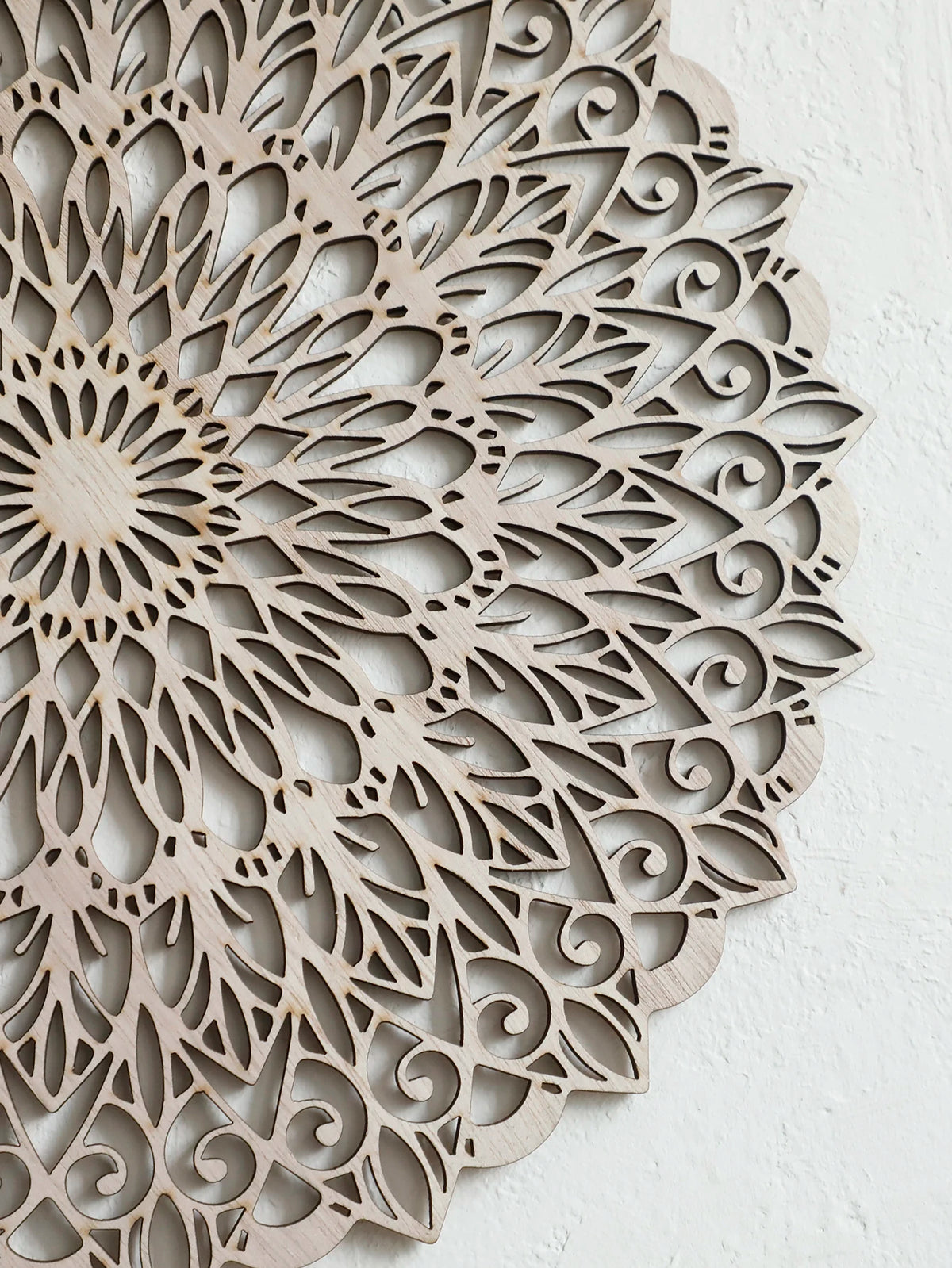 Decoración de pared tipo mandala de madera clara con intrincados recortes en patrón floral circular.
