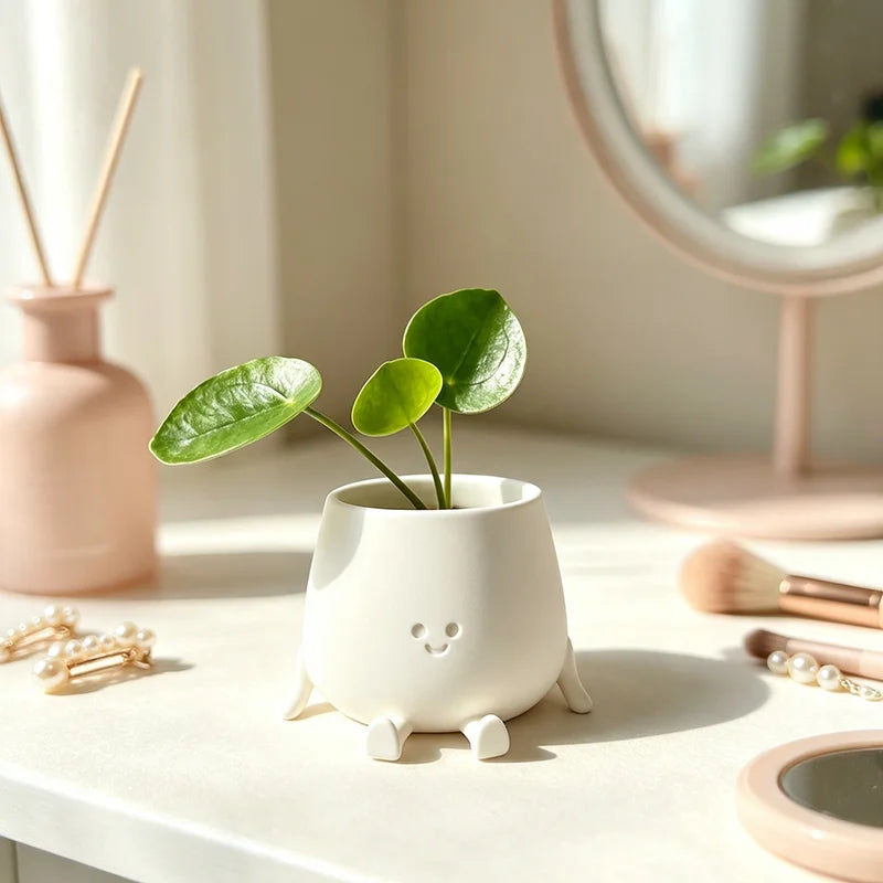 A white 3D printed smiley face succulent planter holding a green plant on a light surface.