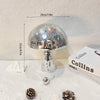 A silver, mushroom-shaped disco ball decoration with a textured surface is displayed on a white surface.