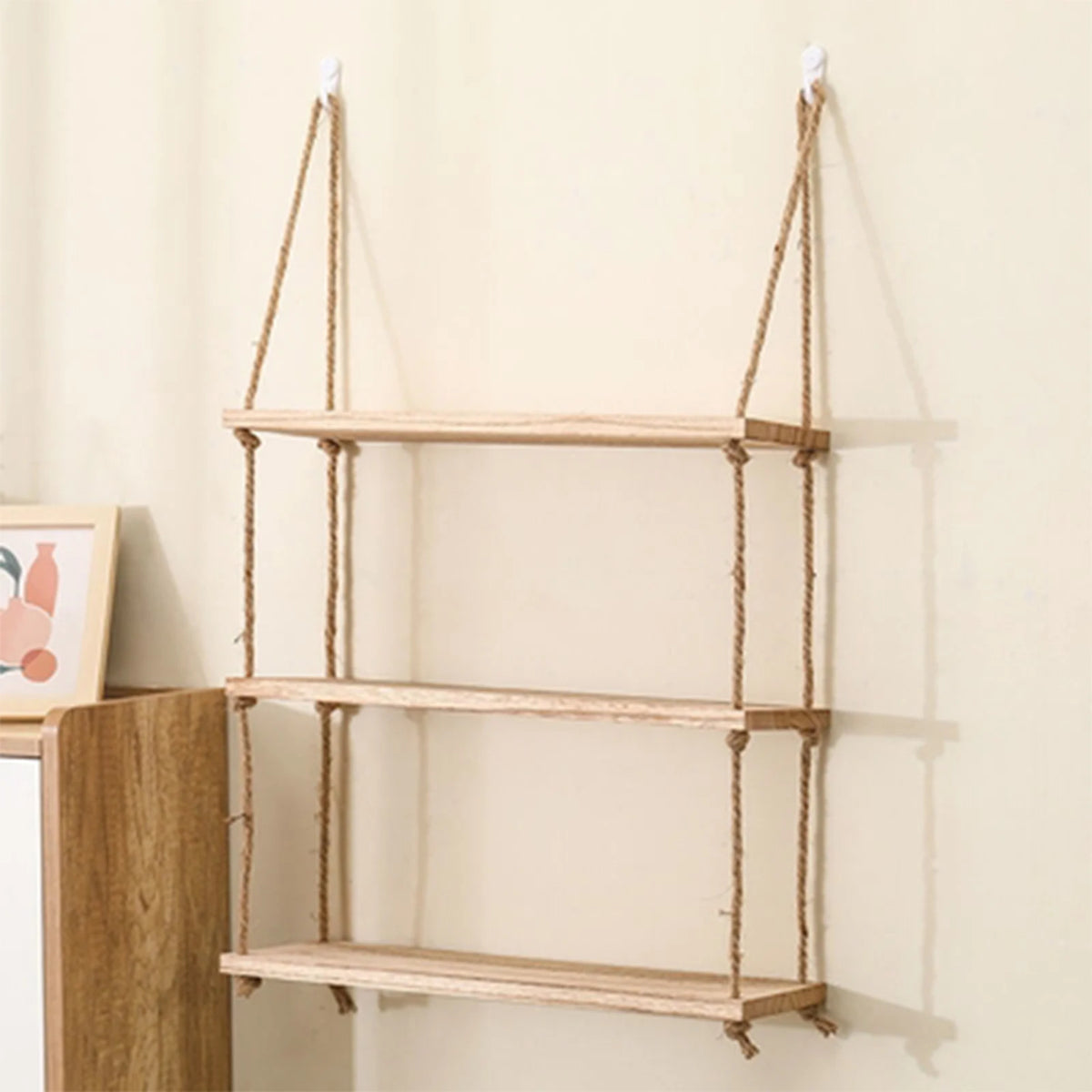 A rustic floating wooden storage shelf with three shelves is mounted on a wall using twine hangers.