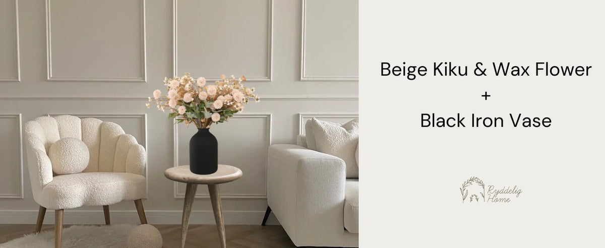 Beige Kiku and Wax Flower arrangement in a black iron vase displayed in a light-colored room.