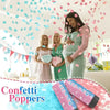 A pregnant woman smiles while two friends toss pink and blue confetti poppers in the air.
