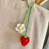 Hand-knitted hanging plant basket with a white flower and a red strawberry hanging from a beige fabric