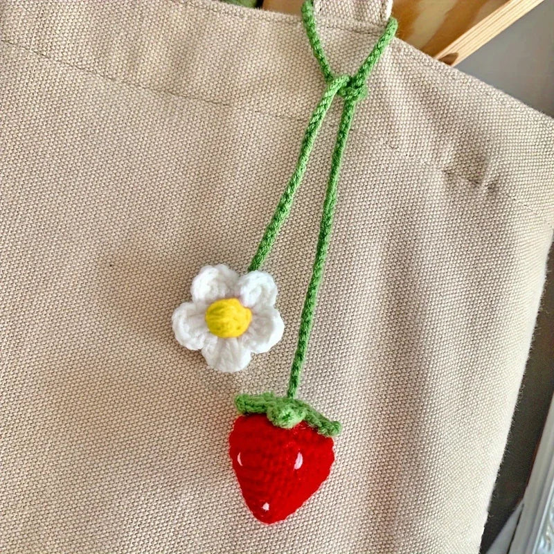 Hand-knitted hanging plant basket with a white flower and a red strawberry hanging from a beige fabric