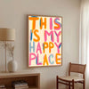 Impresión en lienzo enmarcada con el texto "This is my happy place" en tipografía colorida en una pared blanca.