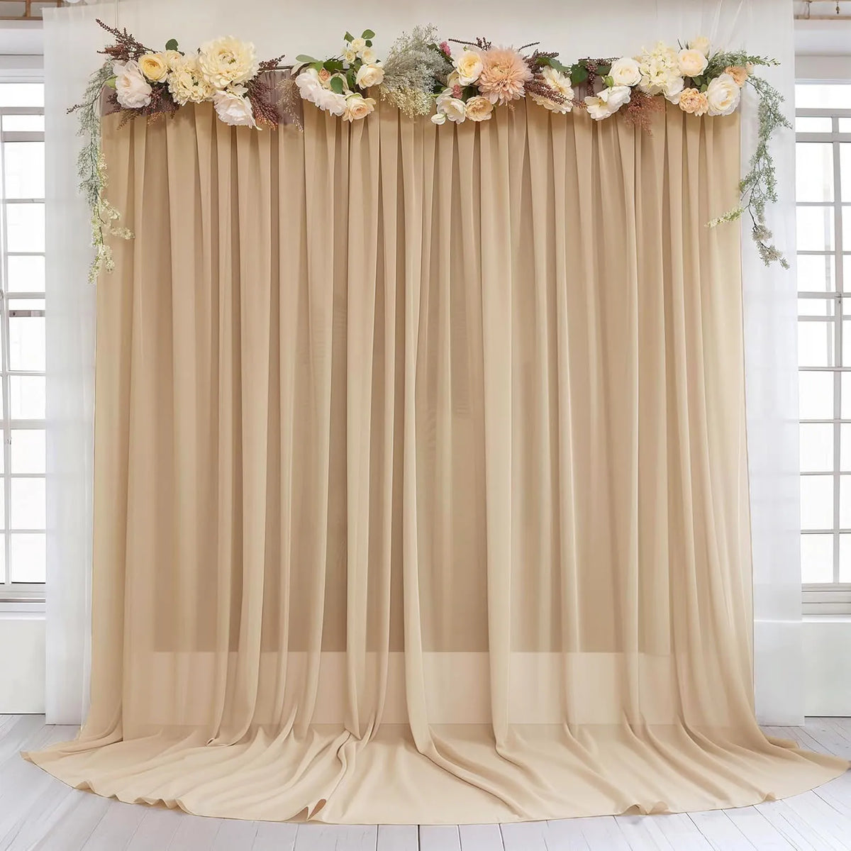 A beige chiffon backdrop curtain decorated with floral greenery and light flowers for wedding or event decor.