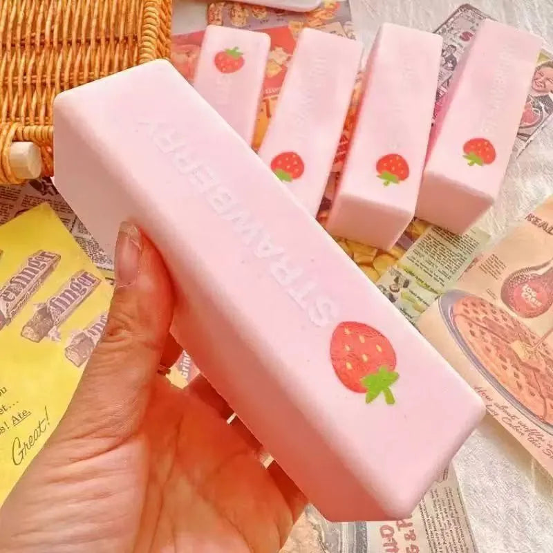 A hand holds a pink strawberry-shaped butter squeeze toy for stress relief, surrounded by similar items.