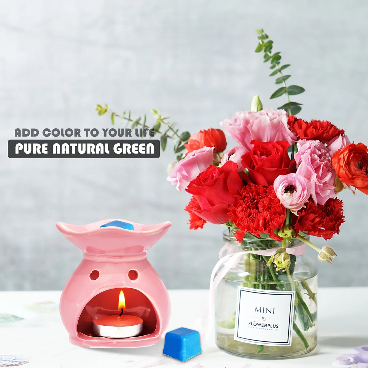 A pink ceramic owl candle holder with a lit tea light sits next to a glass jar of pink and red floral arrangement.