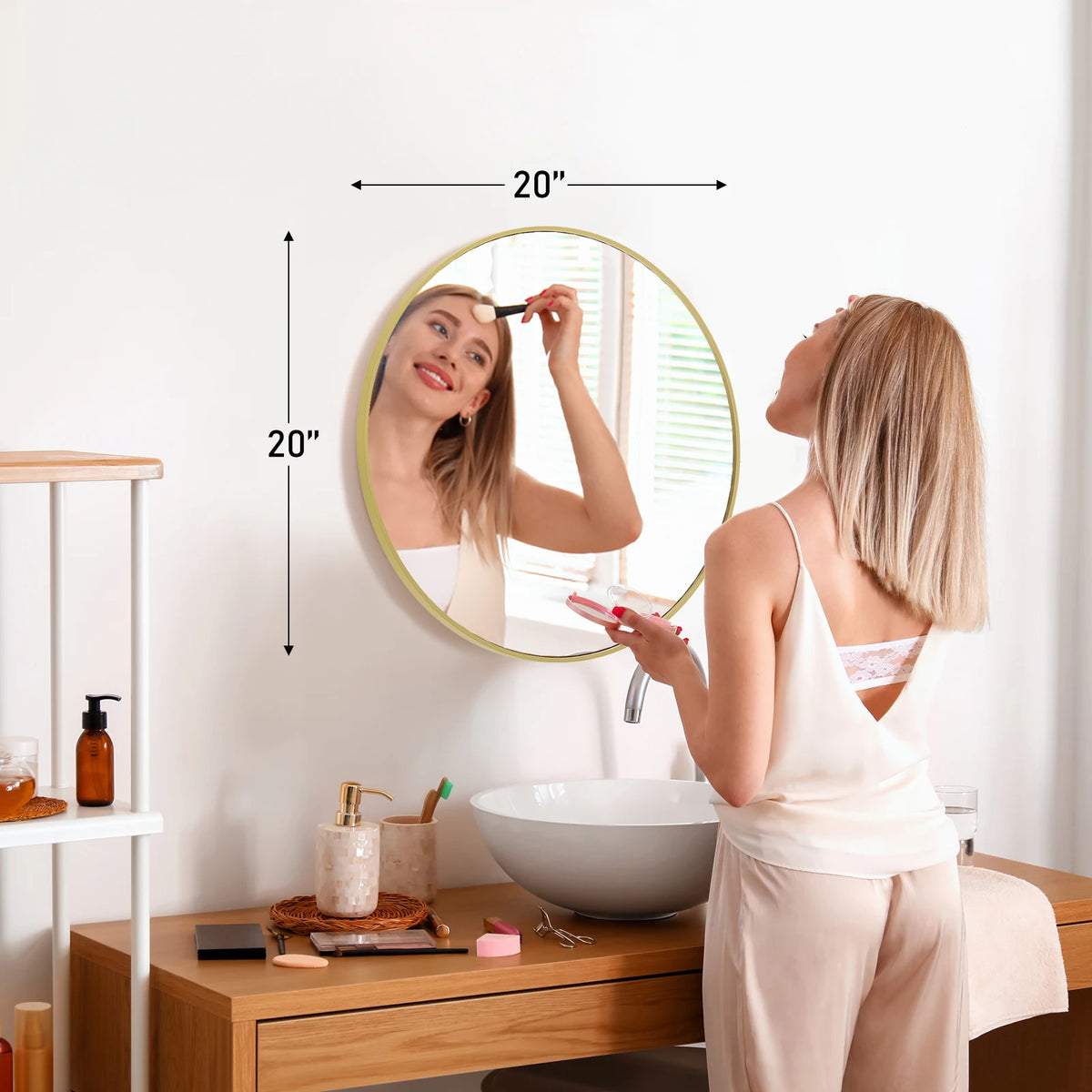 A woman is looking in a large round vanity mirror with a matte metal frame in a bright bathroom setting.