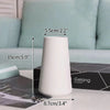 A white ceramic bud vase with a tapered shape is shown on a table next to product dimensions.