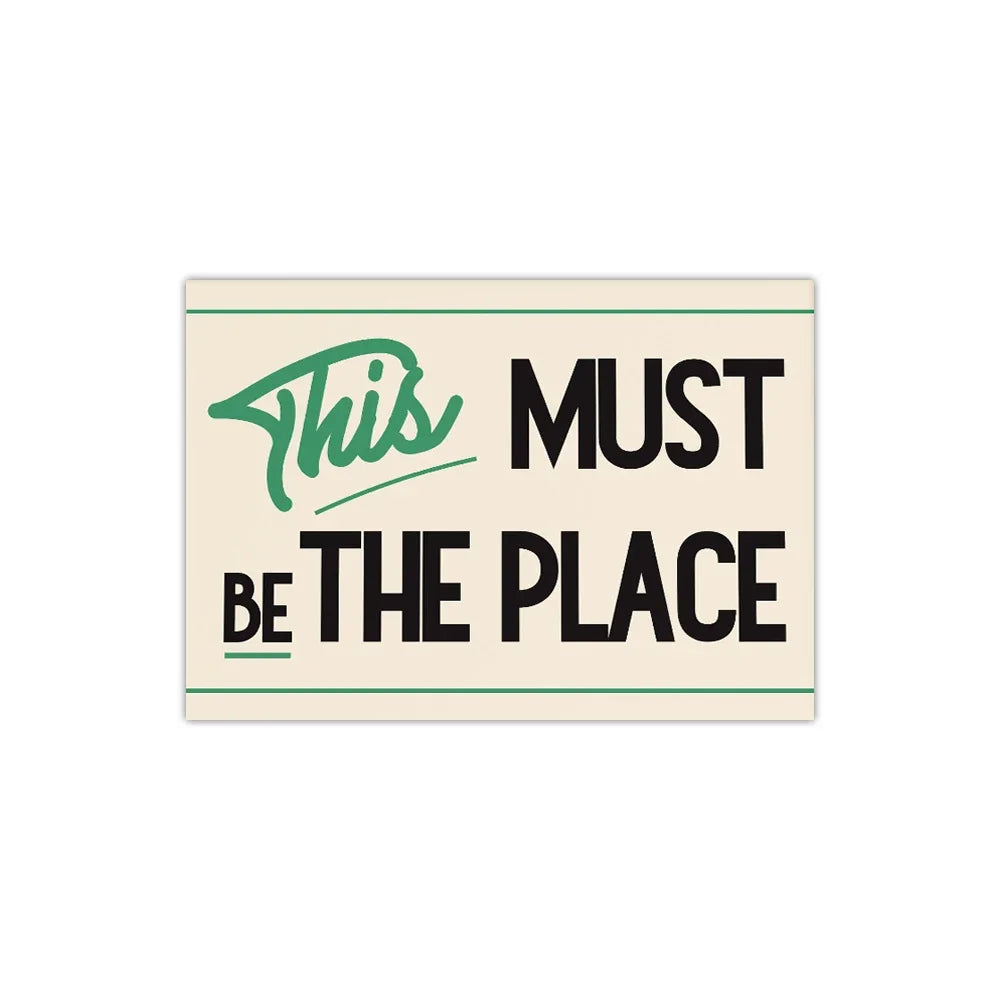 Wall art featuring the text This Must Be The Place in green and black on a beige background.