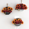 Trois arrangements de tournesols artificiels et de fleurs rouge foncé exposés sur un mur blanc.