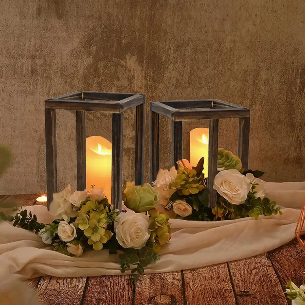 A rustic wooden candle holder lantern with a glowing candle and floral arrangement on a wooden surface.
