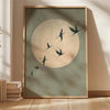 A framed canvas wall art featuring a large pale circle with several dark silhouettes of cranes flying across it.