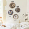 A collection of round boho straw wall hangings in various sizes and patterns displayed on a light-colored wall.