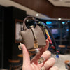 A hand holds a mini house handbag with a gold clasp and wrist strap against a dark background.