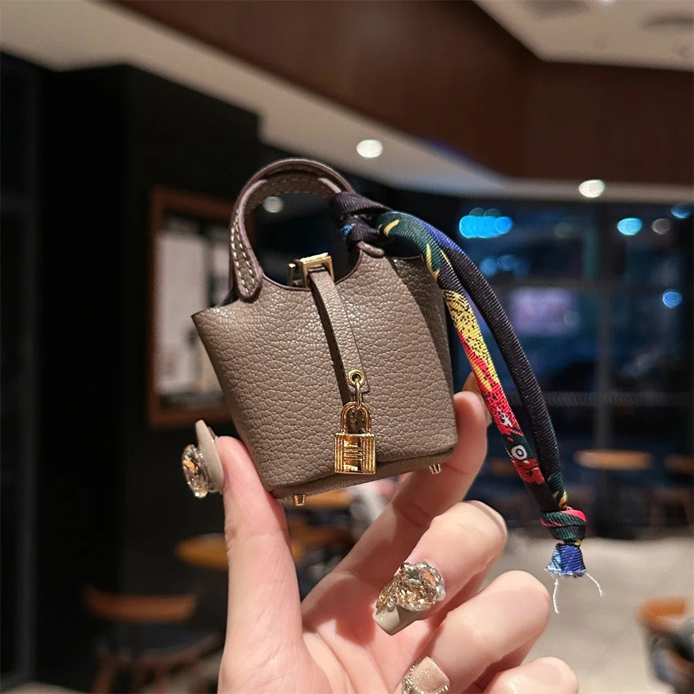 A hand holds a mini house handbag with a gold clasp and wrist strap against a dark background.