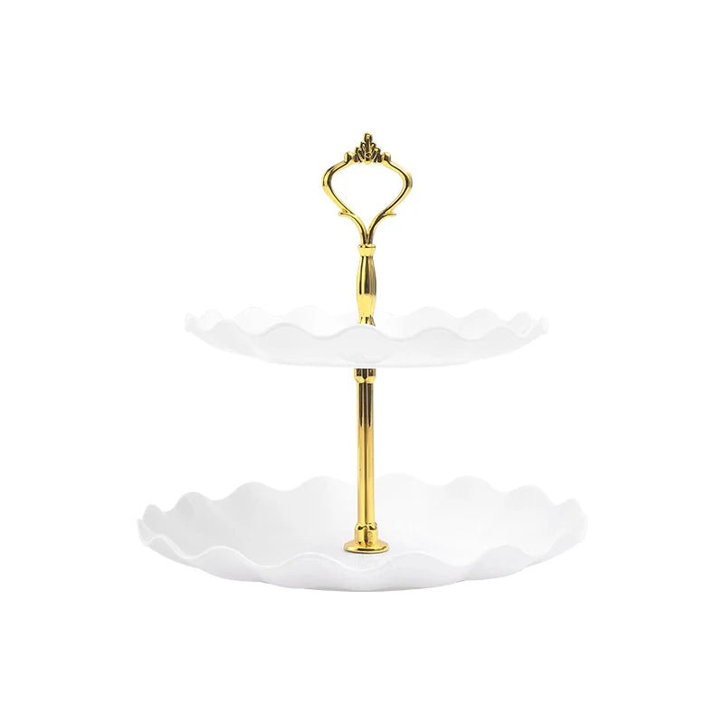 A gold two-tier serving stand with white scalloped dishes for desserts and fruit.