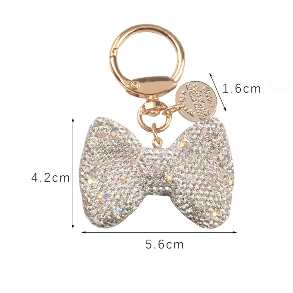 A sparkling rhinestone bow keychain with a gold-toned ring and a circular charm.