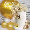 A white cake decorated with gold leaf and pearl accents, surrounded by gold and white balloons.